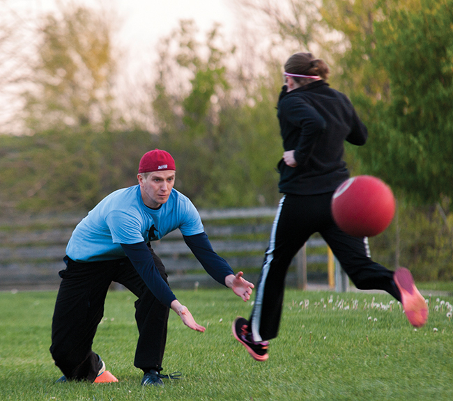 David Berning of team Sloth Lodge prepares for the catch as Katrina Folsom of Kickin’ up Daisies crosses first base during Thursday night kickball at Olcott Park. Photo by Darryl Smith