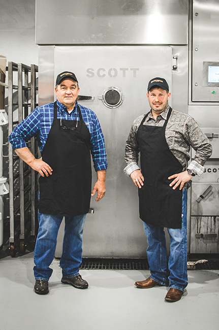 Jim Wells (left) and Greg Stube in front of the Wagon Wheel’s computerized smokehouse. Photo by Aubrey Dunnuck 