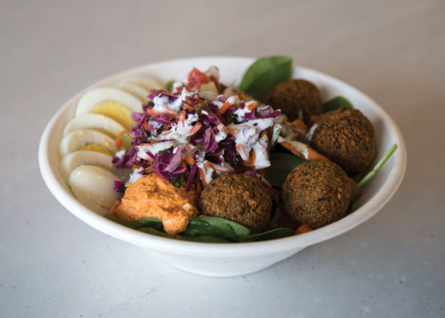 A falafel bowl with egg, Israeli salad, spiced carrots, red cabbage slaw, and Greek yogurt and herb dressing. 